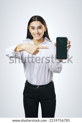 Mobile application concept with happy girl in white shirt showing modern cellphone with blank screen on abstract light background, mockup