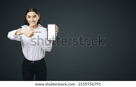 Mobile application concept with happy girl in white shirt showing modern smartphone with white blank screen on abstract dark background with place for your logo or text, mock up