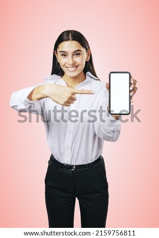Mobile application concept with happy girl in white shirt showing modern cellphone with white blank screen on abstract pink background, mockup