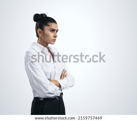Resentment and unpleasant emotions concept with stressed young woman in white shirt crossing her arms isolated on light grey background, close up