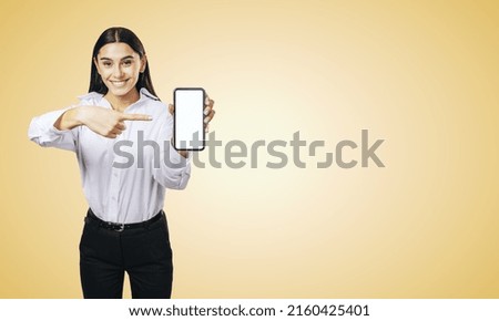 Mobile application concept with smiling businesswoman in white shirt showing modern smartphone with white blank screen on abstract orange background with place for your logo or text, mock up