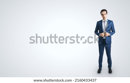 Young self-confident businessman in blue suit and grey tie isolated on light grey wall background with blank place for your logo, mockup