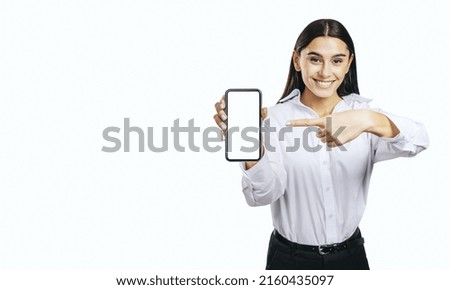 Mobile application concept with happy girl in white shirt showing modern smartphone with white blank screen on abstract light background with place for your logo or text, mock up