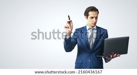Young man in suit with pen in one hand and laptop in another going to write on white background with copyspace for your logo and text, mock up