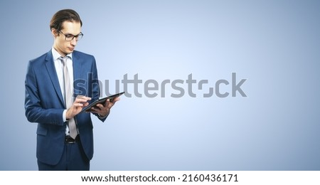 Young businessman in suit with digital tablet on light blue background with place for your text, mock up