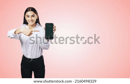 Mobile application concept with smiling businesswoman in white shirt showing modern cellphone with blank screen on abstract light pink background with place for your logo or text, mockup