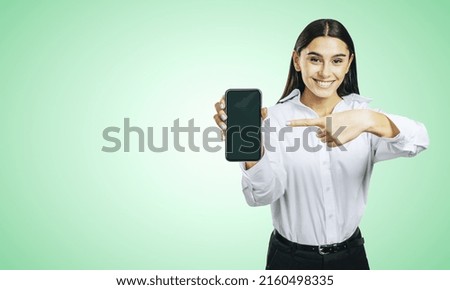 Mobile application concept with happy girl in white shirt showing modern smartphone with blank screen on abstract light green background with place for your logo or text, mock up