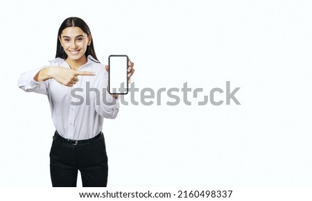 Mobile application concept with smiling businesswoman in white shirt showing modern smartphone with blank white screen isolated on light background with place for your logo or text, mock up