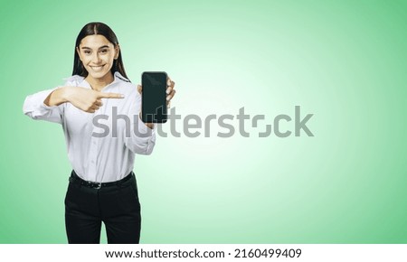 Mobile application concept with happy girl in white shirt showing modern cellphone with blank screen on abstract light green background with place for your logo or text, mockup