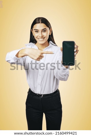 Mobile application concept with happy girl in white shirt showing modern cellphone with blank screen on abstract light orange background, mockup