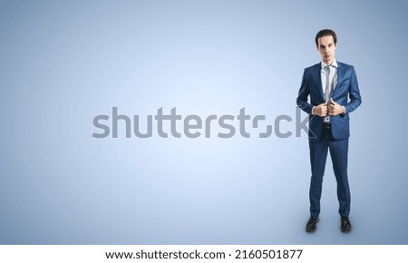 Young self-confident businessman in blue suit and grey tie isolated on light blue wall background with blank place for your logo, mockup