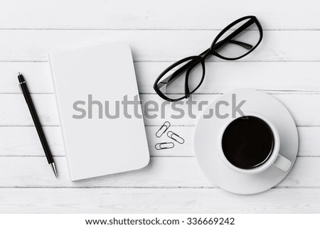 Blank diary, pen, cup of coffee, clips and glasses on white wooden table, mock up