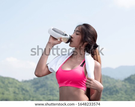 Close up Young asian woman drink water after running on road in the morning sunshine outdoors. Female jogger exercising. Fitness and healthy lifestyle