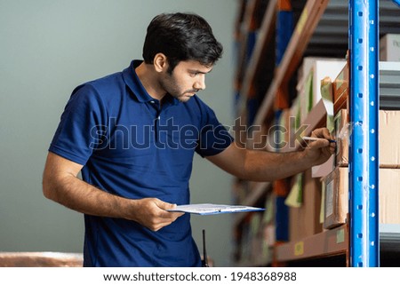 Male employee warehouse worker using clipboard checking products or parcel goods on shelf pallet in industry factory warehouse. Inspection quality control