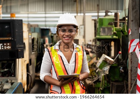 Factory woman worker at work in the industry factory, work with digital tablet with happy and smile. Female worker maintaining machine in the industrial plant
