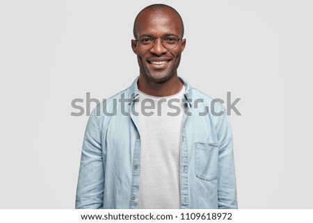 Horizontal shot of happy dark skinned male with positive smile on face, being in high spirit as achieves success in business sphere, dressed in casual outfit, isolated over white background.