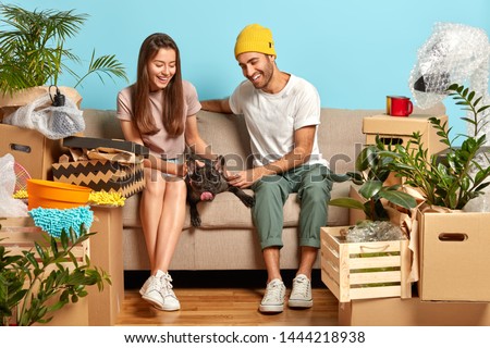 Affectionate newlywed married couple care about french bulldog, pose together on couch, enter own house for first time, rest on sofa in living room, have happy expressions, have day of relocation.