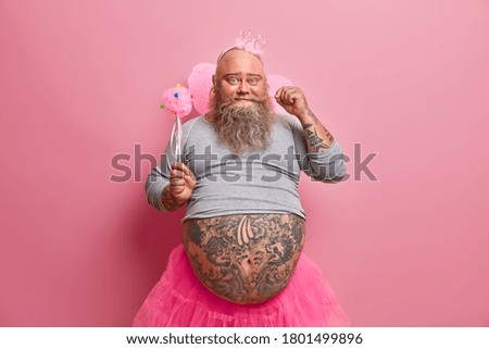 Handsome positive fat man curls mustache, has fun on party, feels like real princess, wears crown, wings, organises baby shower for her newborn daughter. Beared fatso fairy has childish mood