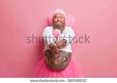 Male performer or holiday animator works on party for little children, has funny expression, holds magic wand, dressed like fairy, isolated on pink background, wears fancy wings. Man from wonderland