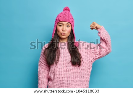 Une femme brune sérieuse lève le bras et montre des muscles confiants en eux-mêmes et pleins de puissance porte un saut à couteaux roses qui se sent en bonne santé isolé sur fond bleu. Regardez mes biceps