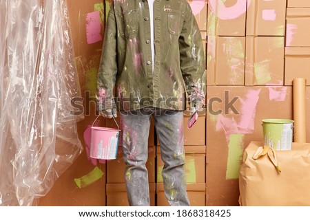Cropped image of man painter holds bucket of pink paint and brush does quick repair of house finishes painting walls in room wears casual shirt and jeans. Maintenance and home improvement concept