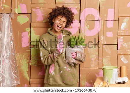 Happy dark skinned young woman does repairs in apartment has fun after painting walls sings in paint brush relocates at new house busy doing room renovation. Home improvement and repair concept