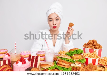 Una mujer asiática seria con labios rojos piel sana sostiene deliciosos nuggets que comen deliciosos aperitivos adictos a la comida rápida usa albornoz suave y toalla sobre la cabeza aislada sobre fondo blanco. Comida para picar