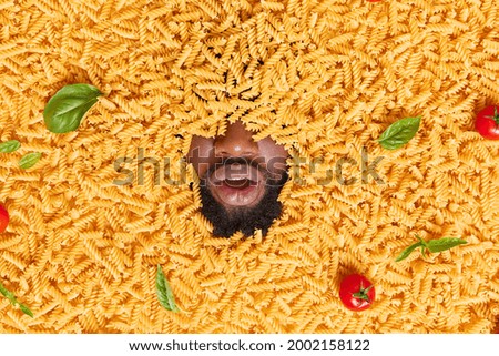 Mans head posing through raw pasta with red tomatoes green basil leaves going to cook delicious supper. Ingredients for tasty dinner. Italian cuisine concept. People food nutrition. Cooking process