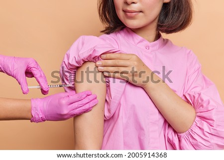 Cropped shot of unrecognizable woman does vaccination in clinic wears pink blouse cares about her health during pandemic. Female patient receives covid 19 vaccine. Population immunization campaign