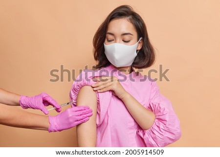 Cute suspicious Asian girl with short hair, comes to the vaccination centre in a mask, wants to protect her family and agrees on injection. Does not want it to hurt and does not believe her doctor.