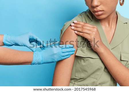 Population immunization concept. Unrecognizable woman gets injection against coronavirus wears dress isolated over blue studio background. Unknown nurse in medical gloves makes shot vaccination