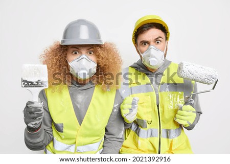 Repair and building concept. Srunned female and male workers hold painting brush and roller work on apartment improvement wear protective respirator and uniform isolated over white background
