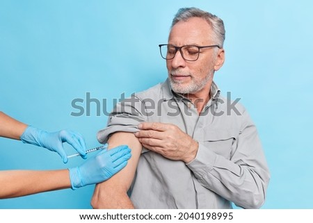 Unrecognizable doctor makes injection to senior patient. Elderly man gets antiviral vaccine at health center during immunization campaign. Successful covid 19 vaccination. Disease prevention