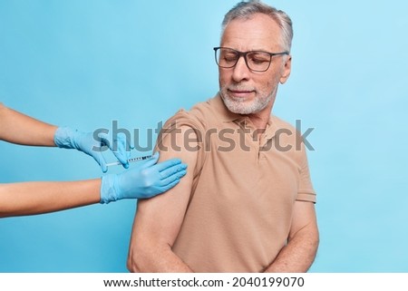 General practitioner vaccinates old male model gives injection against coronavirus. Bearded mature man cares about health gets vaccine to protecrt himself from flu or covid 19. Time to vaccinate