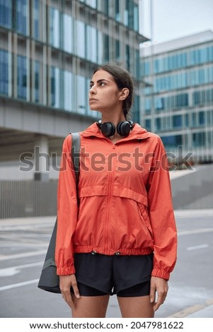 Outdoor shot of young motivated woman in sportswear carries fitness mat trains in morning has workout session poses against blurred city background thinks how to improve health and be active