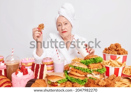 Un régime alimentaire rapide. Une femme senior sérieusement ridée boit un cocktail mange des nuggets a des habitudes de suralimentation saute régime porte une serviette de bain enveloppée sur la tête isolée sur fond blanc. Produits malsains