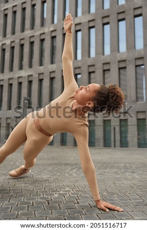 Endurance physical activity and sporty lifestyle concept. Motivated young Afro American woman raises arms exersises poses in plank stengthens core muscles improves stability poses in downtown