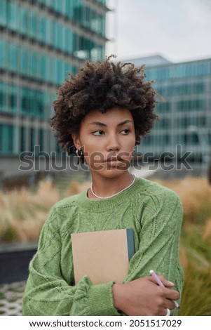 Une travailleuse à distance réfléchie tient un bloc-notes et un stylo écrit des notes dans le planificateur pour faire défiler le projet à l
