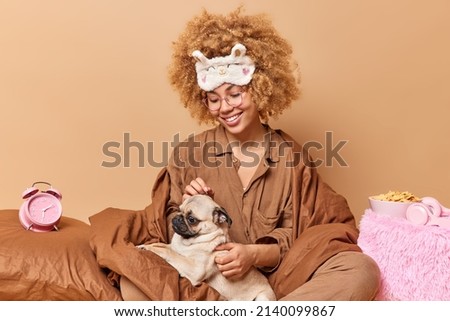 Une jeune femme joyeuse en pyjama doux joue avec un chien préféré au lit le réveil tard a un week-end paresseux à la maison isolée sur fond marron. Un modèle féminin aux cheveux roux et joyeux exprime l