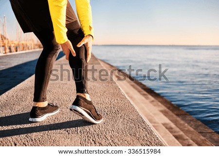 Muscle injury - Athlete running clutching calf muscle after spraining it while out jogging on the beach near ocean. Sports injury concept with running man outside