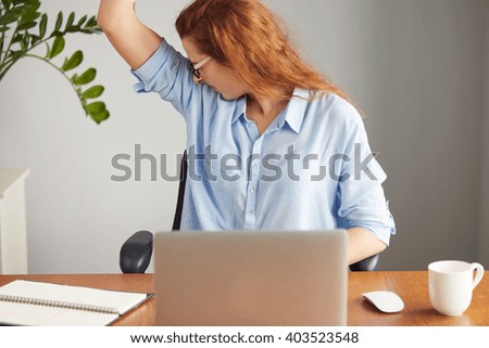 Portrait of a young woman wearing blue shirt disgusting with bad smell of her wet armpit while working in the office. Something stinks, negative human emotions, facial expressions, feeling reaction