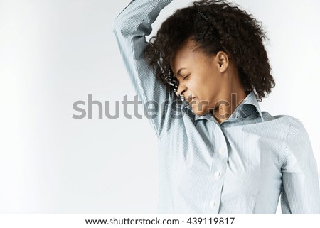 Bad smelling concept. Profile portrait of African woman in striped shirt with black Afro hairstyle, sniffing her armpit with disgusted expression, grimacing, closing her eyes, can't stand stink.