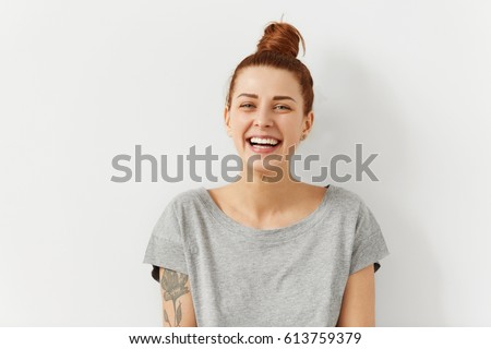Photo of Happy cheerful young woman wearing her red hair in bun rejoicing at positive news or birthday gift, looking at camera with joyful and charming smile. Ginger student girl relaxing indoors after college