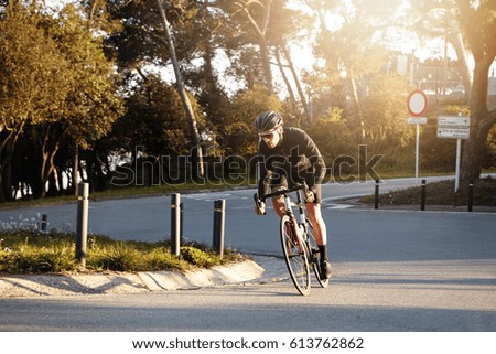 Self-determined professional young cyclist wearing sunglasses and helmet speeding on his racing bike along urban road during cycling race, leaving behind all other athletes, about to win contest