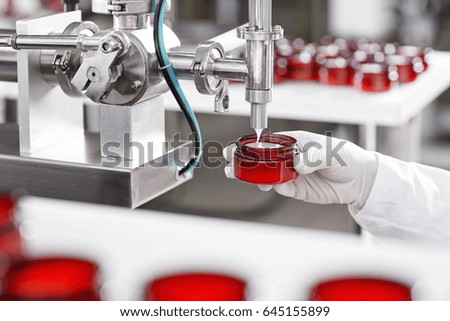 Portrait of big factory process of creating lotion for skincare. Researcher holding container under big metal tube pouring beauty cream isolated over working process at factory and many containers