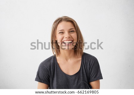 Attractive woman with short fair hair being very glad smiling with broad smile showing her perfect teeth having fun indoors. Joyful excited cheery femlae rejoicing after being proposed to marry