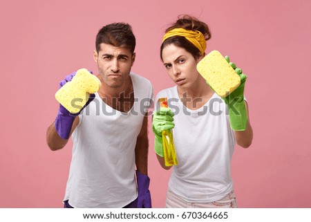 Portrait of scrupulous couple wearing protective gloves and white T-shirts holding sponges and detergent having concentrated look trying to clean everything qualitatively while cleaning windows Stock foto © 