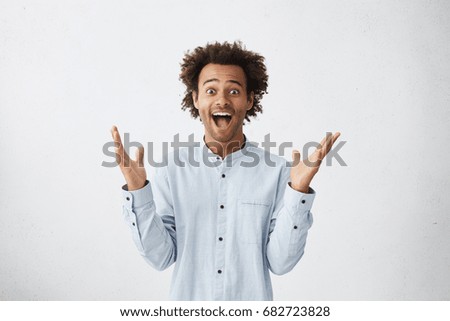 Achievement, success concept. Cheerful Afro American male raising his hands up, having eyes full of happiness rejoicing his great achievements. Attractive black male with curly hair dressed formally