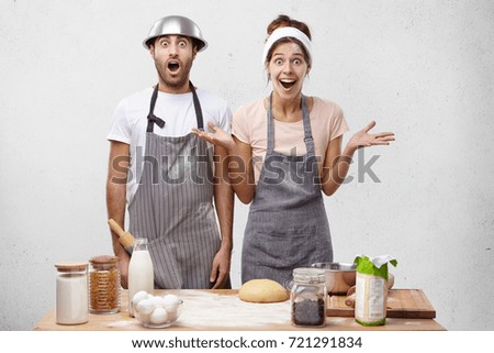 Puzzled family couple bake cookies at kitchen, doesn`t have sugar, gesture with surprisment, not know what to do. Amazed female and male being shocked see guests earlier, hurry to cook dinner