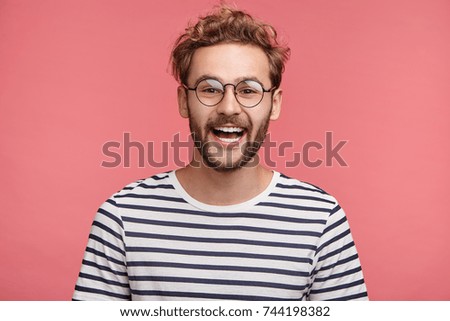 Cheerful hipster guy smiles happily, has excited expression, dresssed casually, celebrates his anniversary or promotion at work, isolated over pink studio background. People, youth, emotions concept